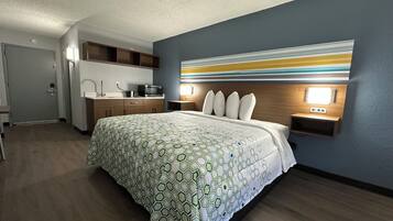 A hotel room with a large bed, a kitchenette, a bathroom, and a decorative wall.