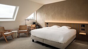 Une chambre d’hôtel moderne dotée d’un grand lit, d’un bureau avec une chaise, d’une petite table et d’une fenêtre laissant entrer la lumière naturelle.