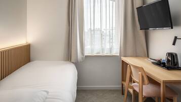 A hotel room with a bed, a desk with a chair, a flat-screen TV, and a window with curtains.