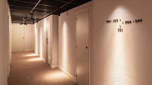 Un couloir avec des portes numérotées, un sol recouvert de moquette et un plafond avec des poutres apparentes.