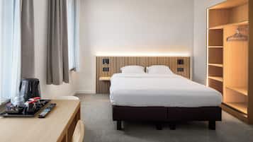 A modern hotel room with a neatly made bed, a wooden desk with a coffee maker, and a large wardrobe.