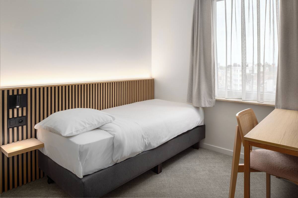 A neatly arranged bedroom with a bed, bedside table, and a chair.