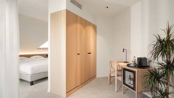 A modern bedroom with a bed, a wooden wardrobe, a desk with a chair, and a potted plant.
