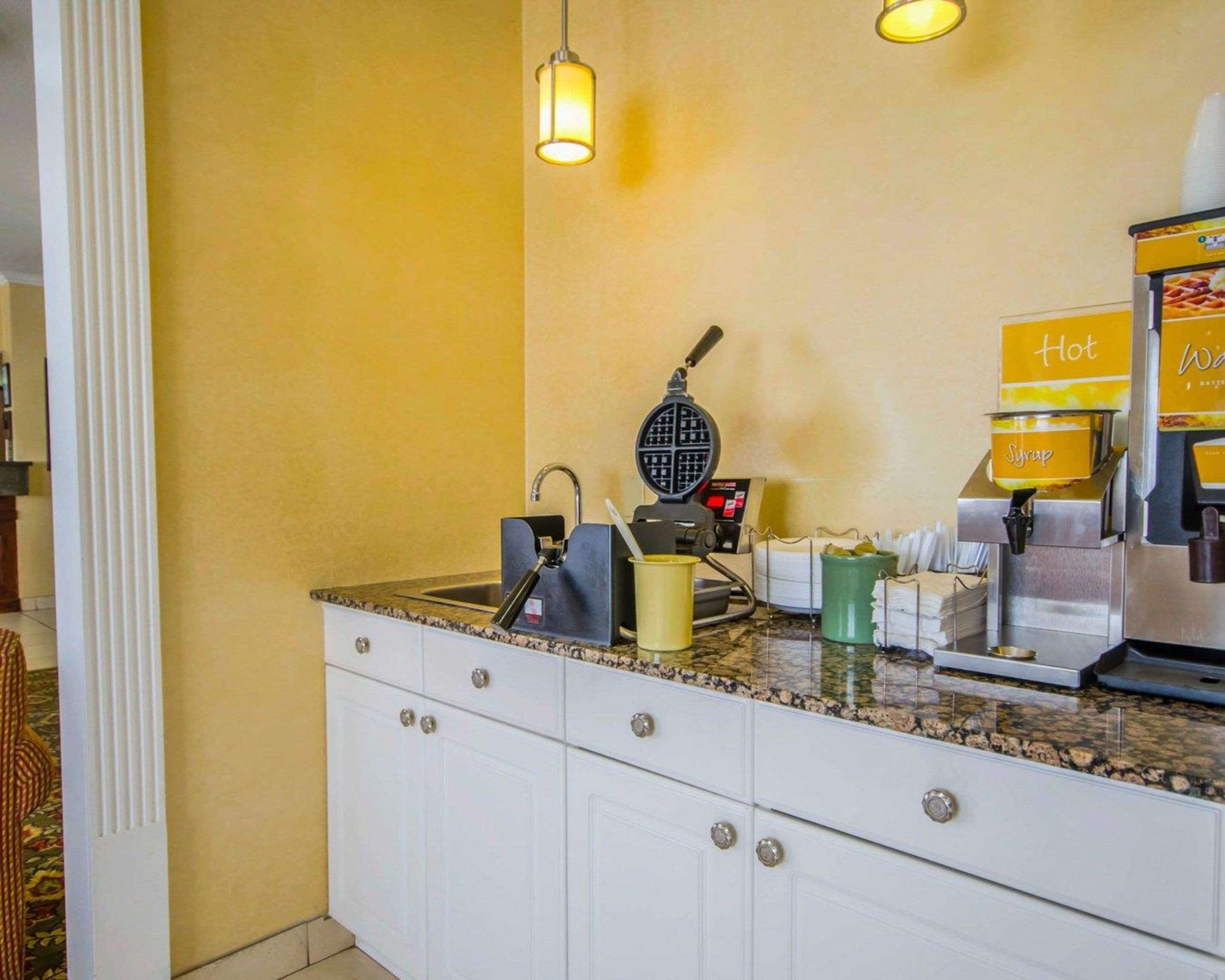 Un área de cocina con una máquina para gofres, dispensador de almíbar y un letrero que indica bebidas calientes.