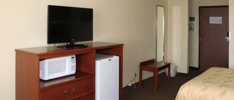 A hotel room with a wooden dresser, a television, a microwave, a refrigerator, a small table, and two beds.