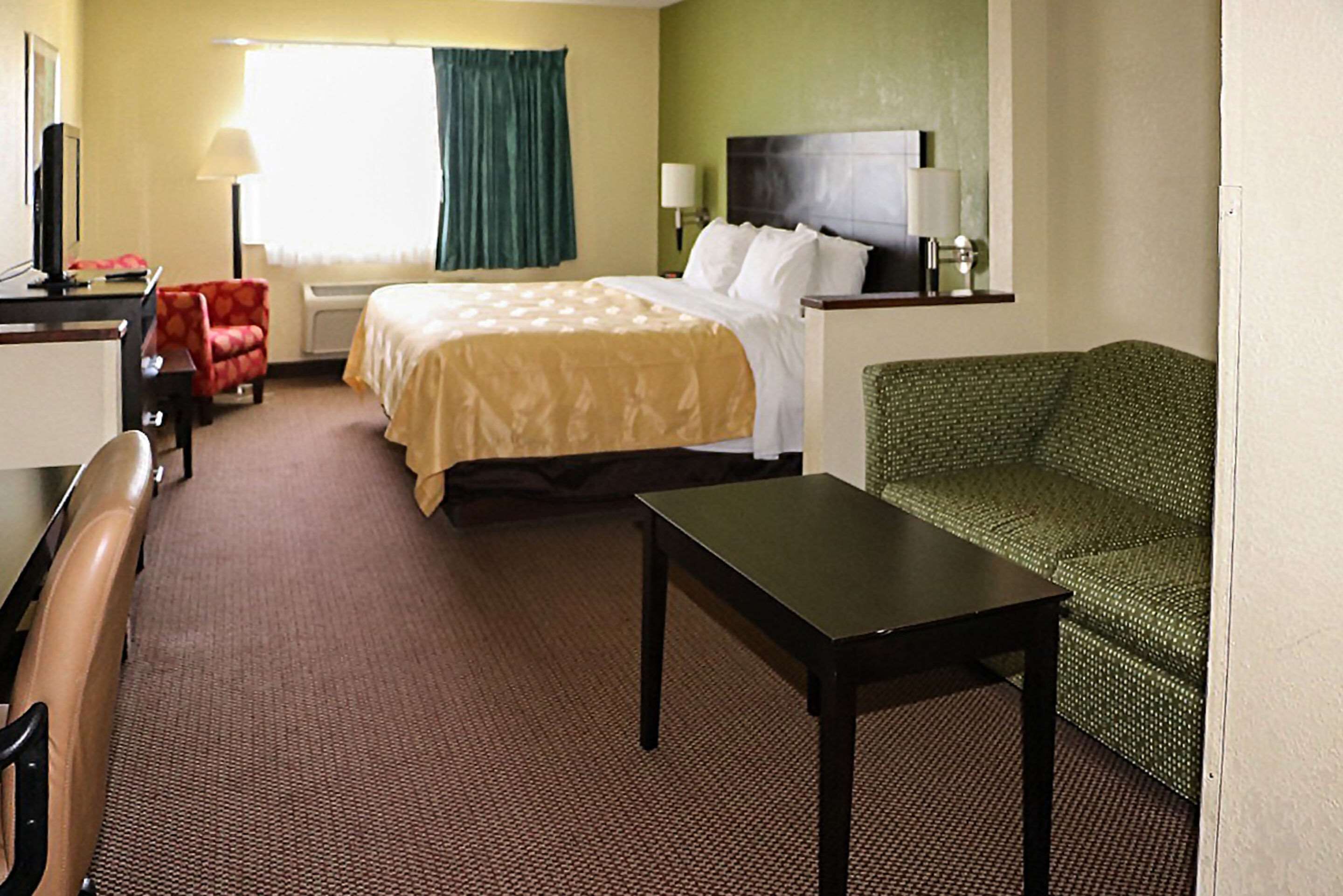 Une chambre d’hôtel avec un lit, un bureau, une chaise, un canapé vert et un téléviseur.