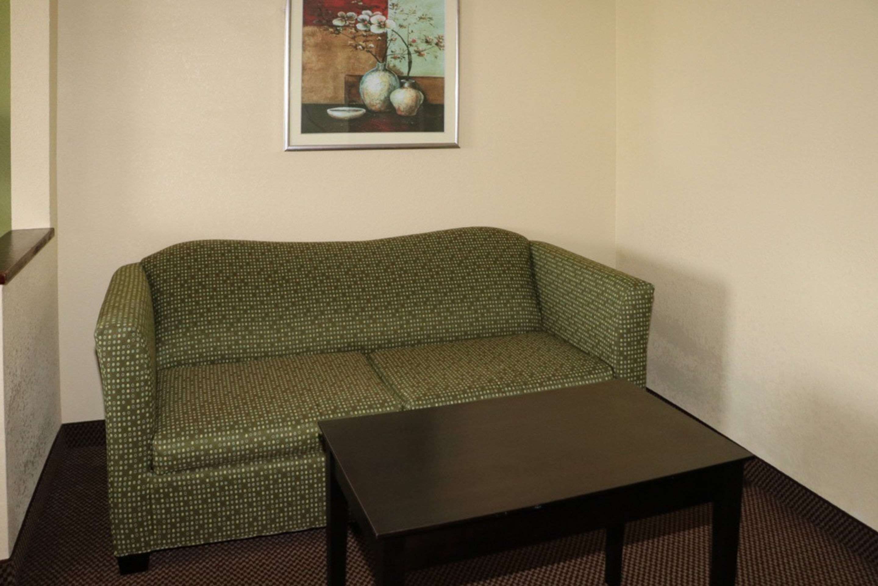 Ein grünes, gemustertes Sofa und ein dunkles Holztablett in einem Raum mit einem gerahmten floralen Kunstwerk an der Wand.