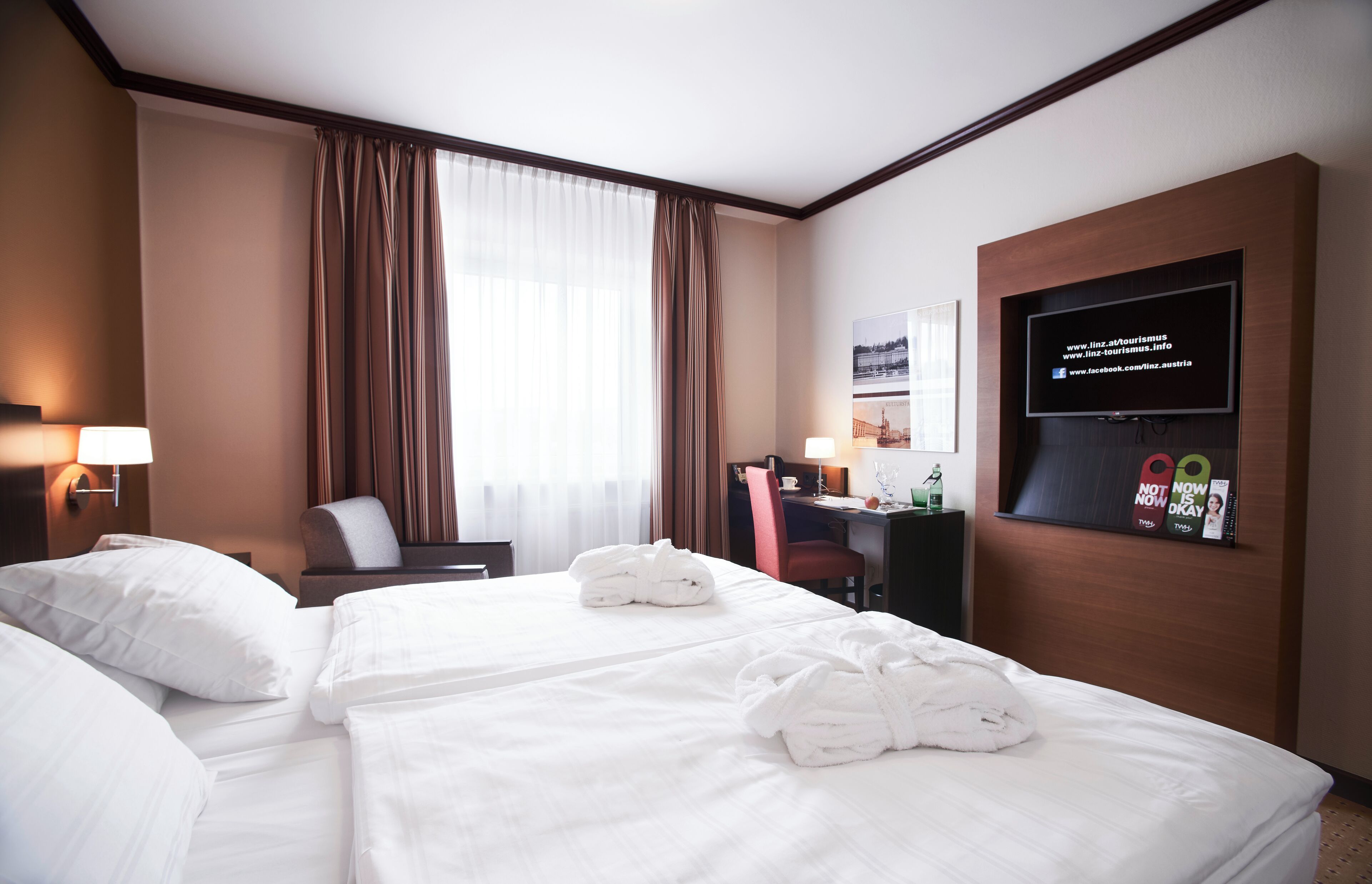 Habitación de hotel con dos camas, un escritorio, una silla, un televisor y una ventana con cortinas.