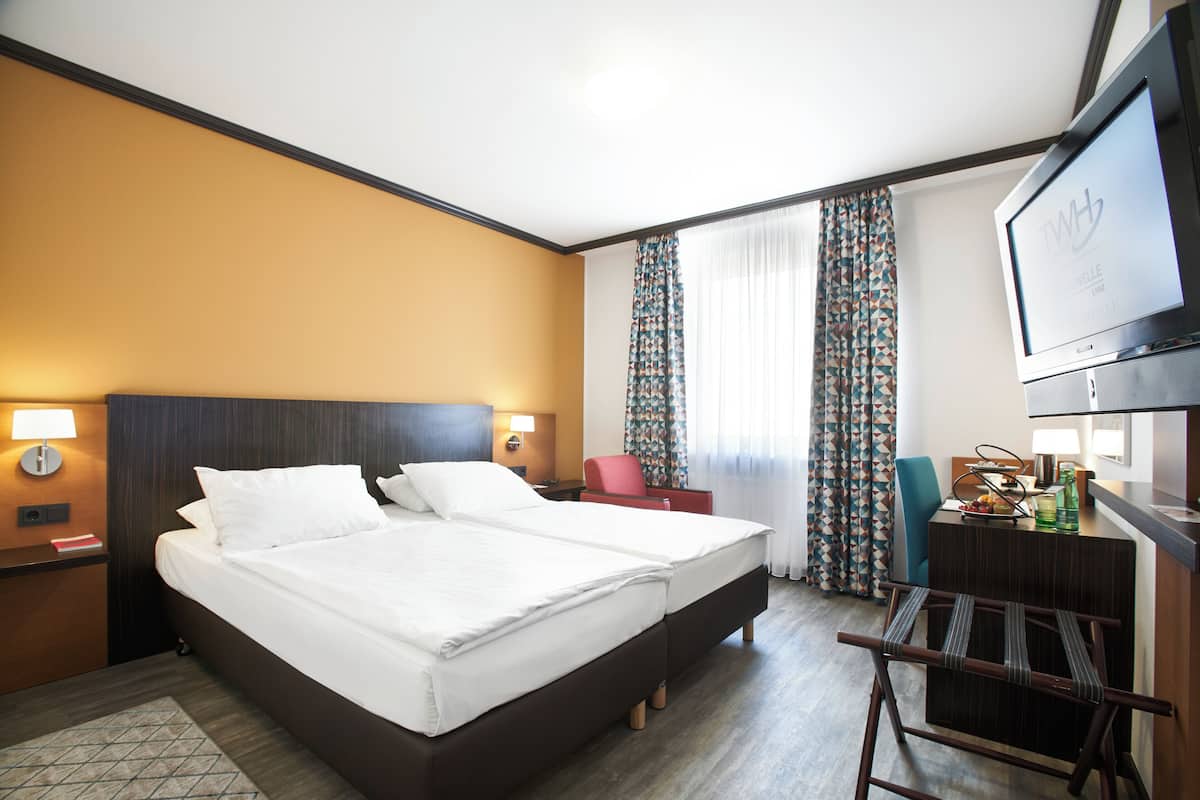 A hotel room with a large bed, a desk, a chair, a TV, and curtains.