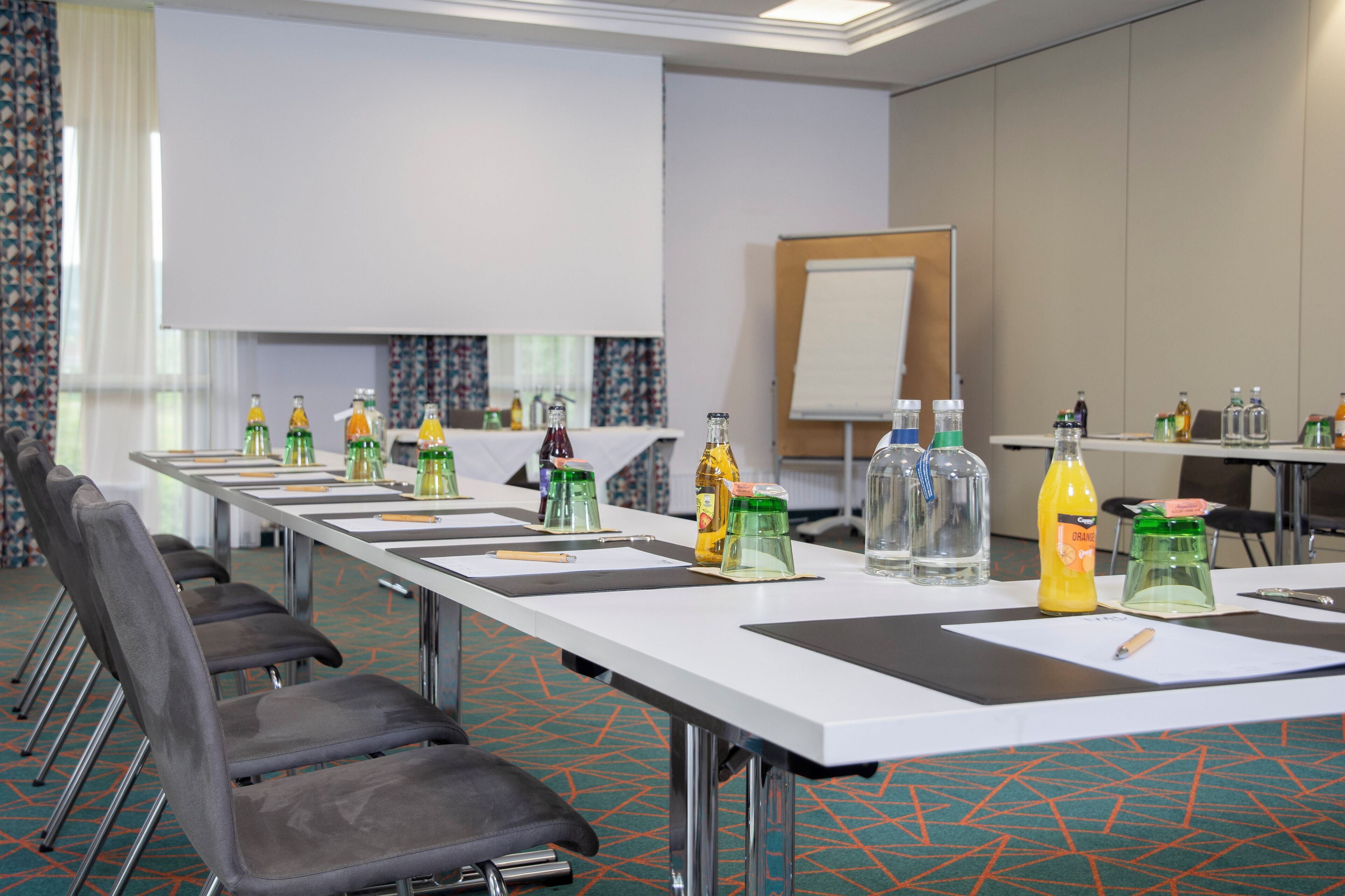 Ein Konferenzraum mit langem Tisch, Stühlen und verschiedenen Getränkeflaschen.