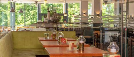 Un restaurante con mesas de madera, asientos con cojines verdes y paneles de vidrio decorativos.