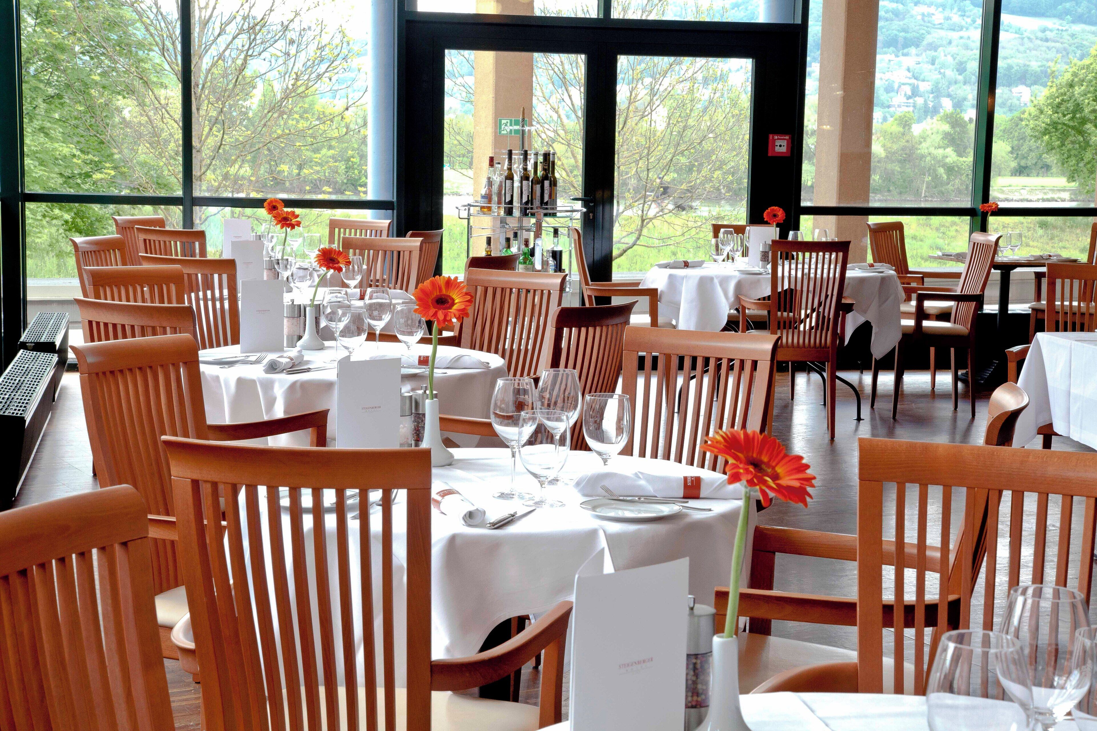 Ein Restaurant mit Holztischen und -stühlen, an jedem Tisch Weingläser und eine Blumenarragemant.