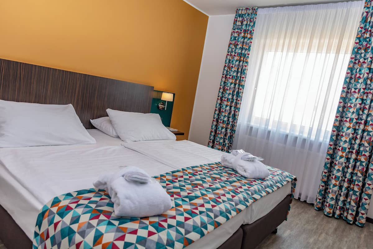A hotel room with a large bed, two pillows, a geometric-patterned bedspread, and a nightstand with a lamp.