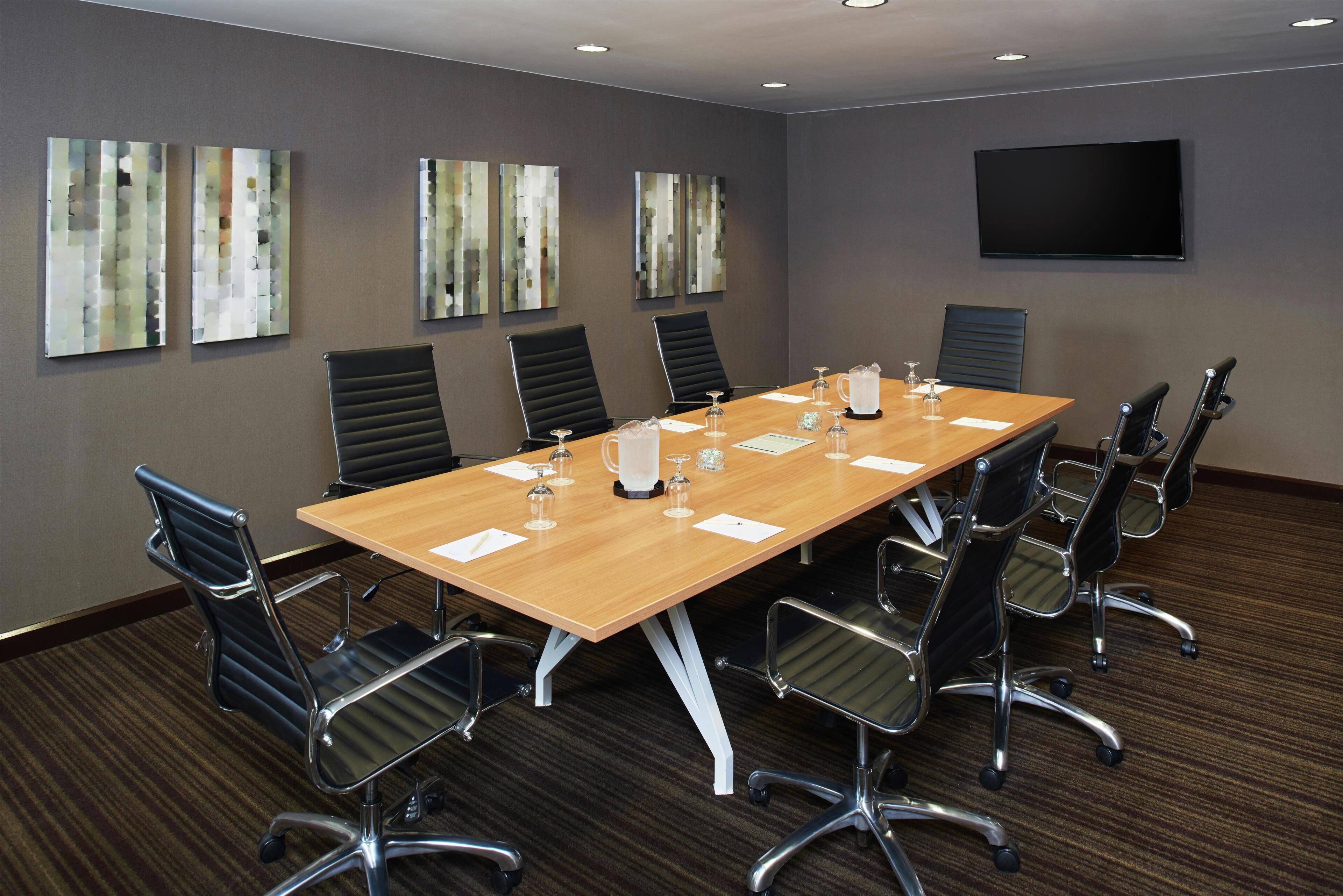 A conference room with a long table, black chairs, a flat-screen TV, and abstract wall art.