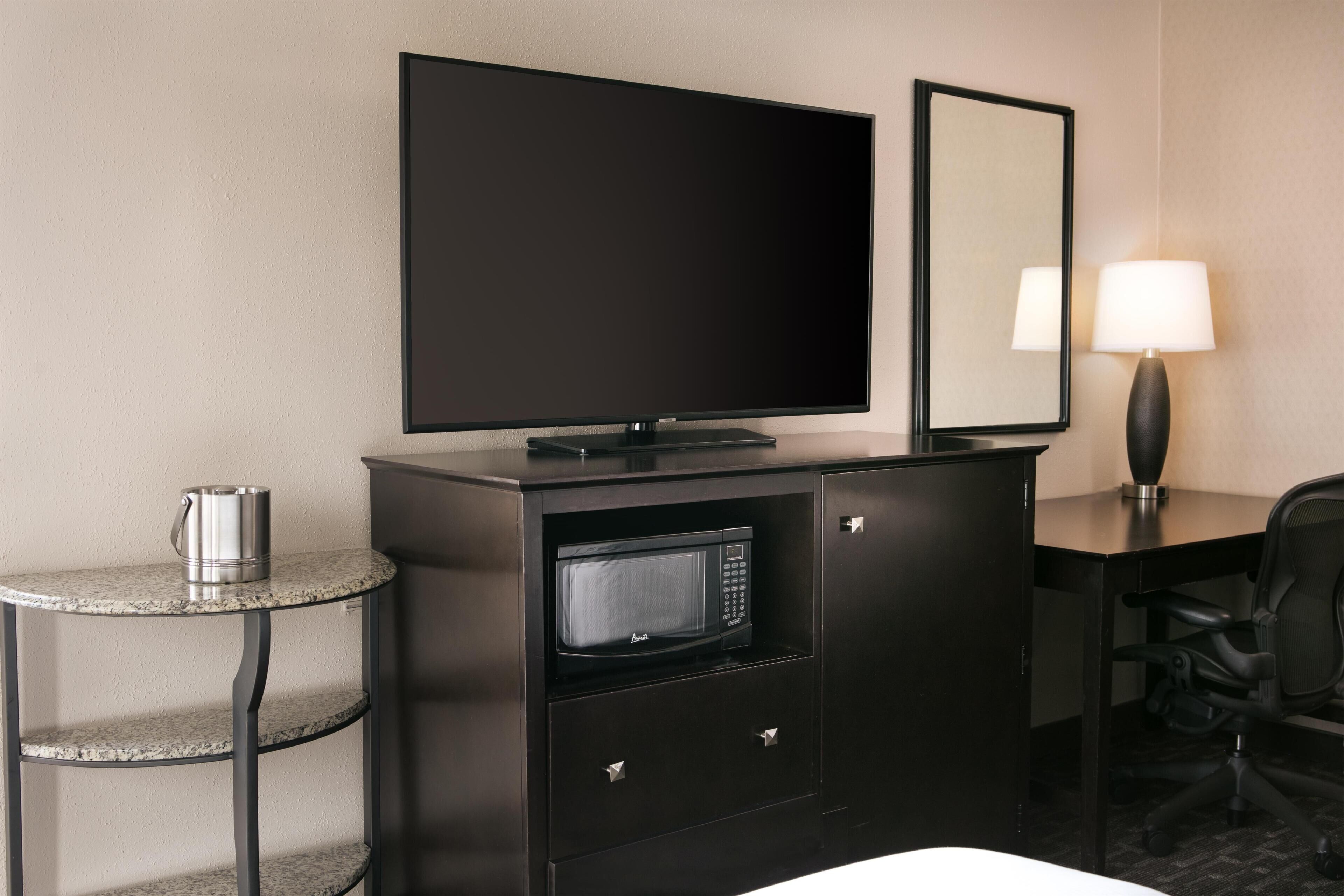 Habitación de hotel con televisión de pantalla plana, microondas, una mesita con hervidor, escritorio con lámpara y una silla.