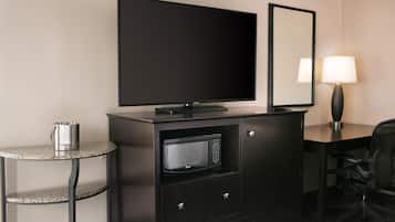 Habitación de hotel con televisión de pantalla plana, microondas, una mesita con hervidor, escritorio con lámpara y una silla.