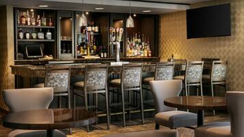 A bar area with multiple seating options, a variety of liquor bottles, and a flat-screen TV mounted on the wall.