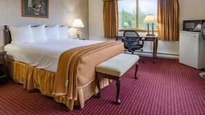 A hotel room with a large bed, a desk, a chair, a television, and a window with curtains. - Travelodge by Wyndham Juneau (Juneau)