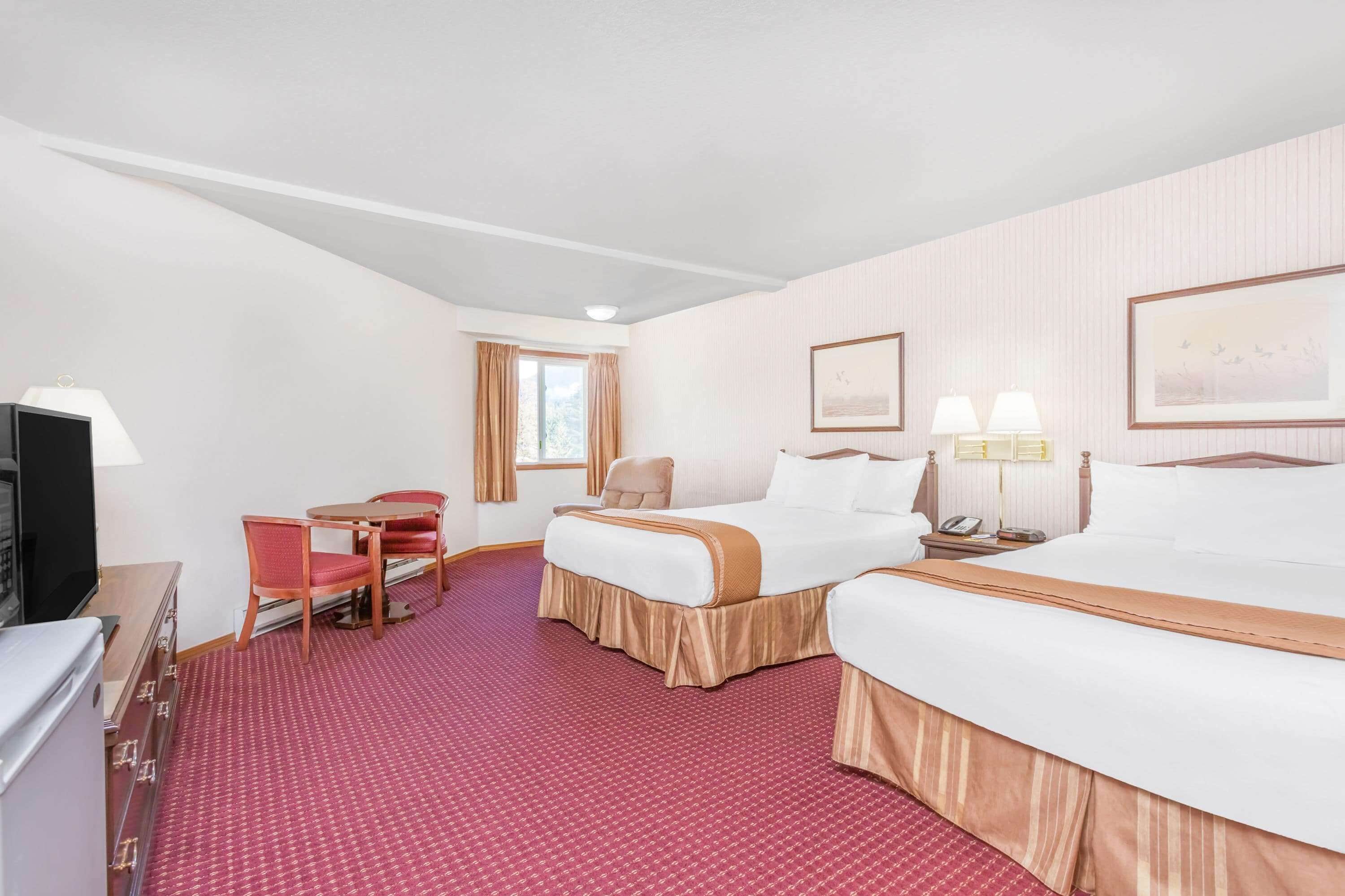 Une chambre d’hôtel avec deux lits, un bureau avec une chaise, une télévision et une fenêtre avec des rideaux.