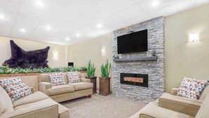 A modern living room with a stone fireplace, beige sofas, and a large bear sculpture. - Travelodge by Wyndham Juneau (Juneau)