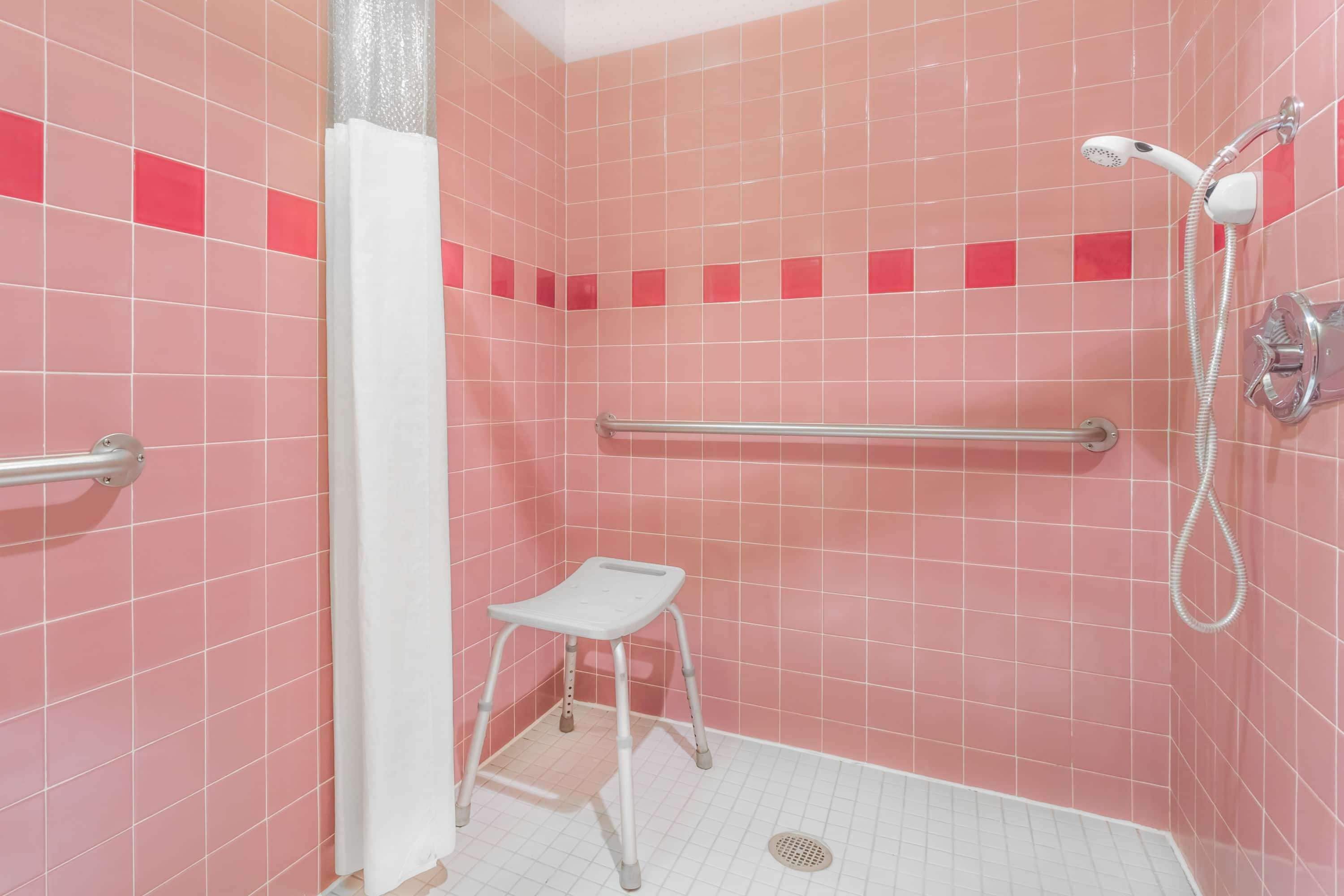 A bathroom with pink tiled walls, a white shower, a grab bar, and a step stool.