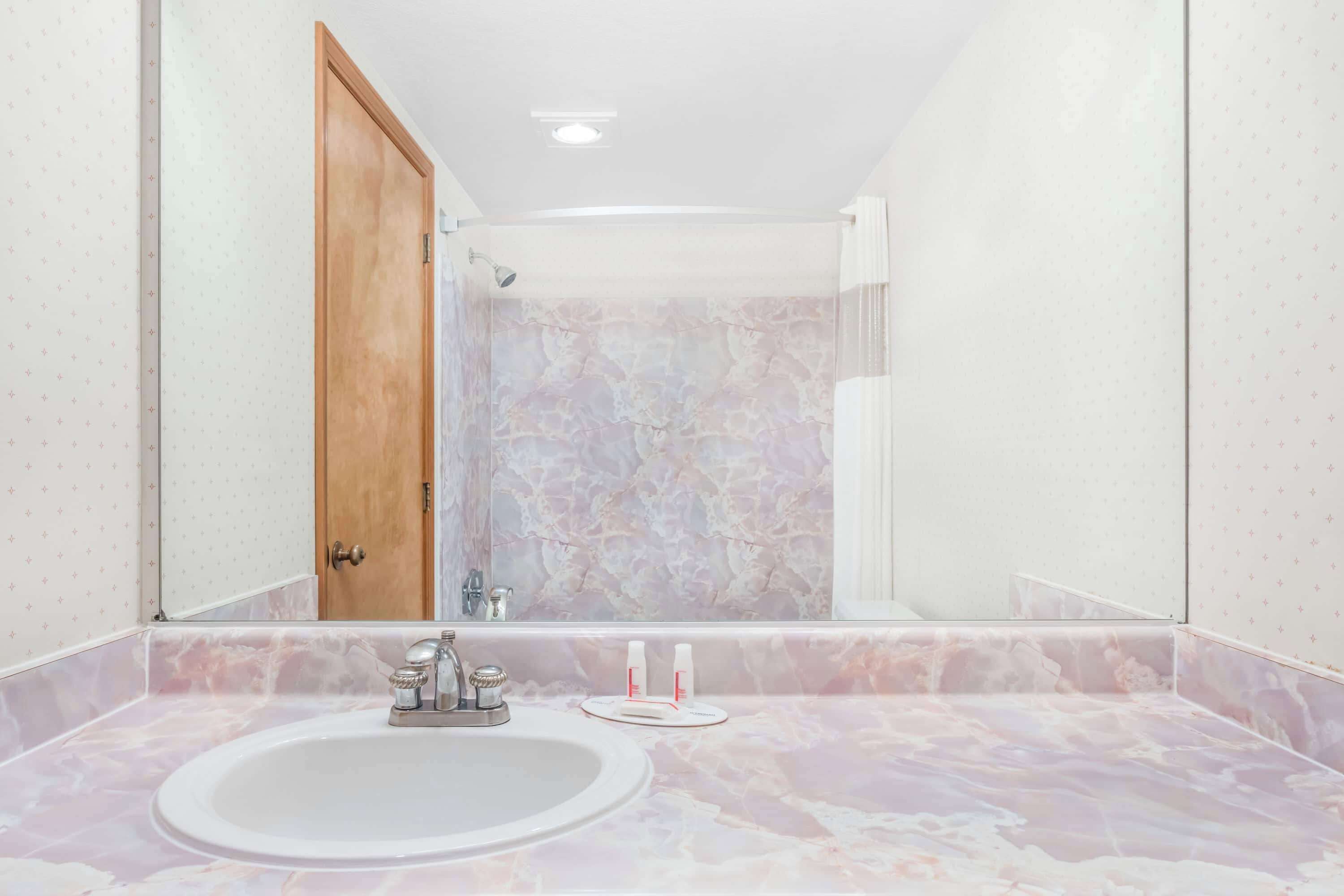 Un baño con lavamanos de mármol, puerta de madera y zona de ducha.