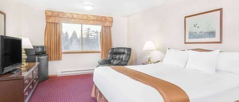 A hotel room with a large bed, a desk with a television, a chair, and a window with curtains.