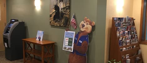 A reception area with a bear mascot, a painting, a desk with a sign, a magazine rack, and an ATM.