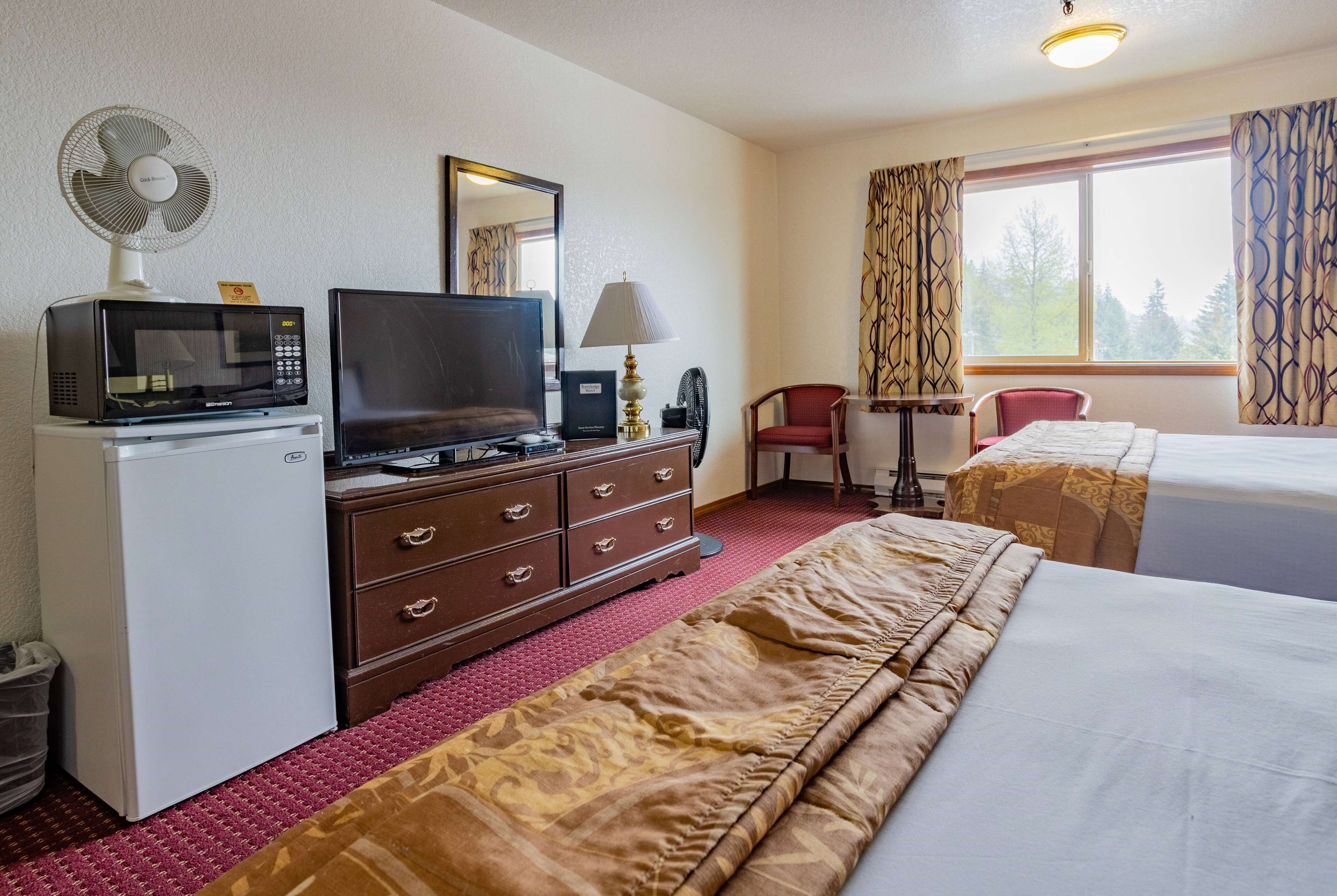 A hotel room with a bed, a desk with a computer, a microwave, a television, and a small fan.