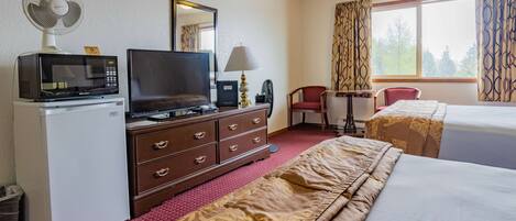Habitación de hotel con cama, escritorio con computadora, microondas, televisor y un pequeño ventilador.