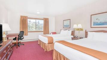 Quarto de hotel com duas camas, uma mesa de escritório com computador, uma cadeira e janela com cortinas.