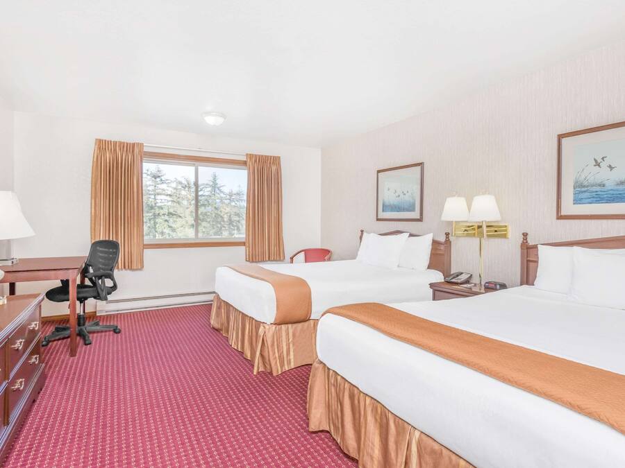 Quarto de hotel com duas camas, uma mesa de escritório com computador, uma cadeira e janela com cortinas.