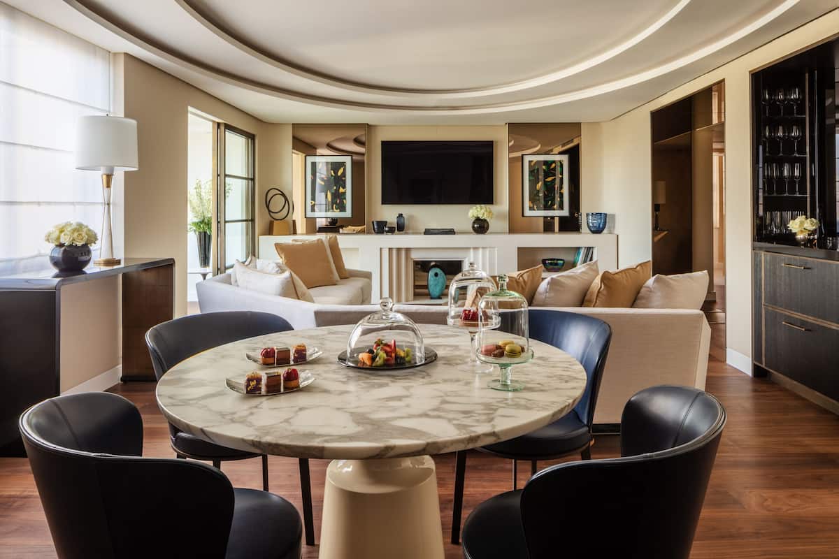 A modern living room with a marble coffee table, leather chairs, a fireplace, and a television.