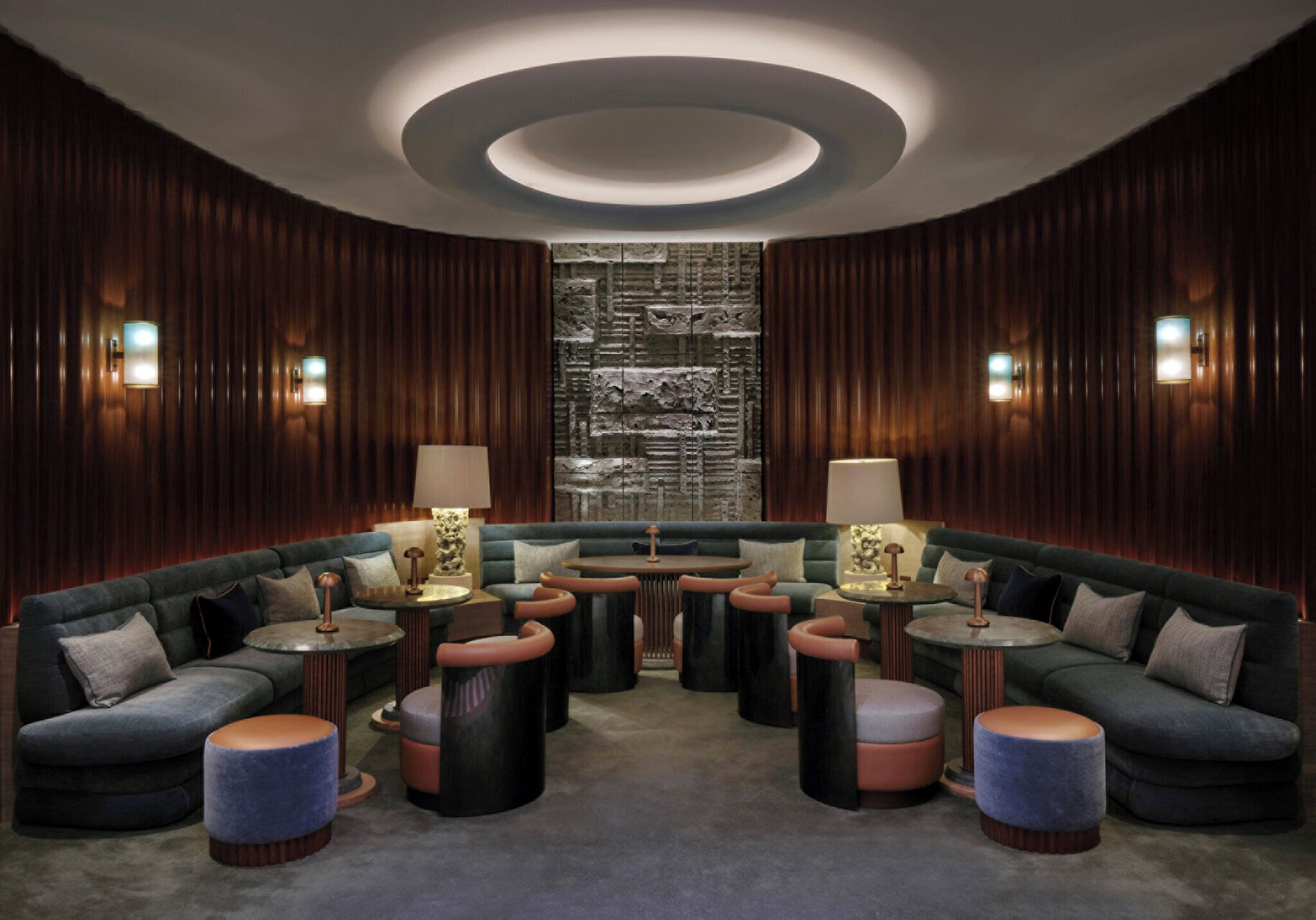 Um lounge moderno com teto curvo, painéis de madeira escura e uma área de estar central com mesas redondas e pufes.