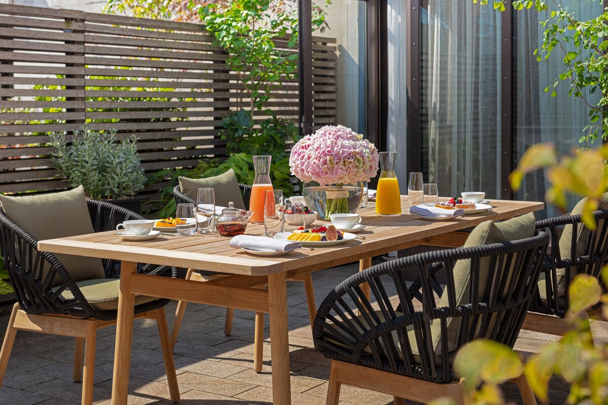 Un espace de restauration en plein air avec une table en bois dressée pour le petit-déjeuner, entourée de chaises en osier.