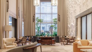 Un hall d  ’entrée spacieux avec une table basse centrale, un coin salon avec des canapés et des fauteuils, de grandes fenêtres donnant sur un immeuble et un mur décoratif orné d’un motif floral.