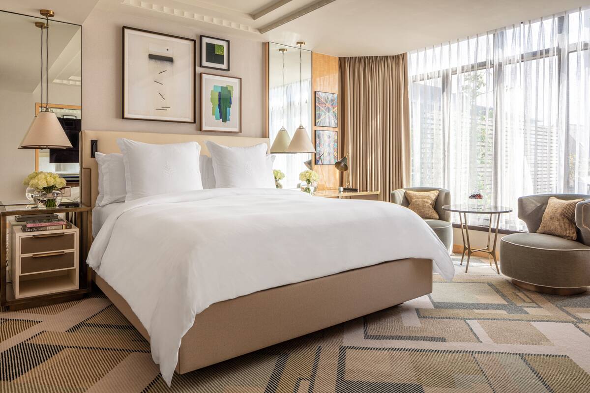 A hotel room with a large bed, bedside tables, a chair, and a small table.