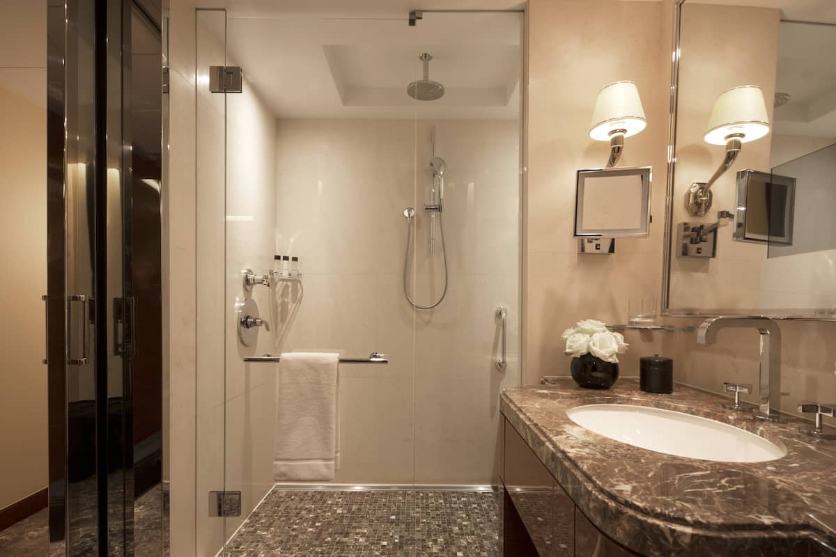 A modern bathroom with a glass-enclosed shower, a marble sink, and a large mirror with wall-mounted lights.