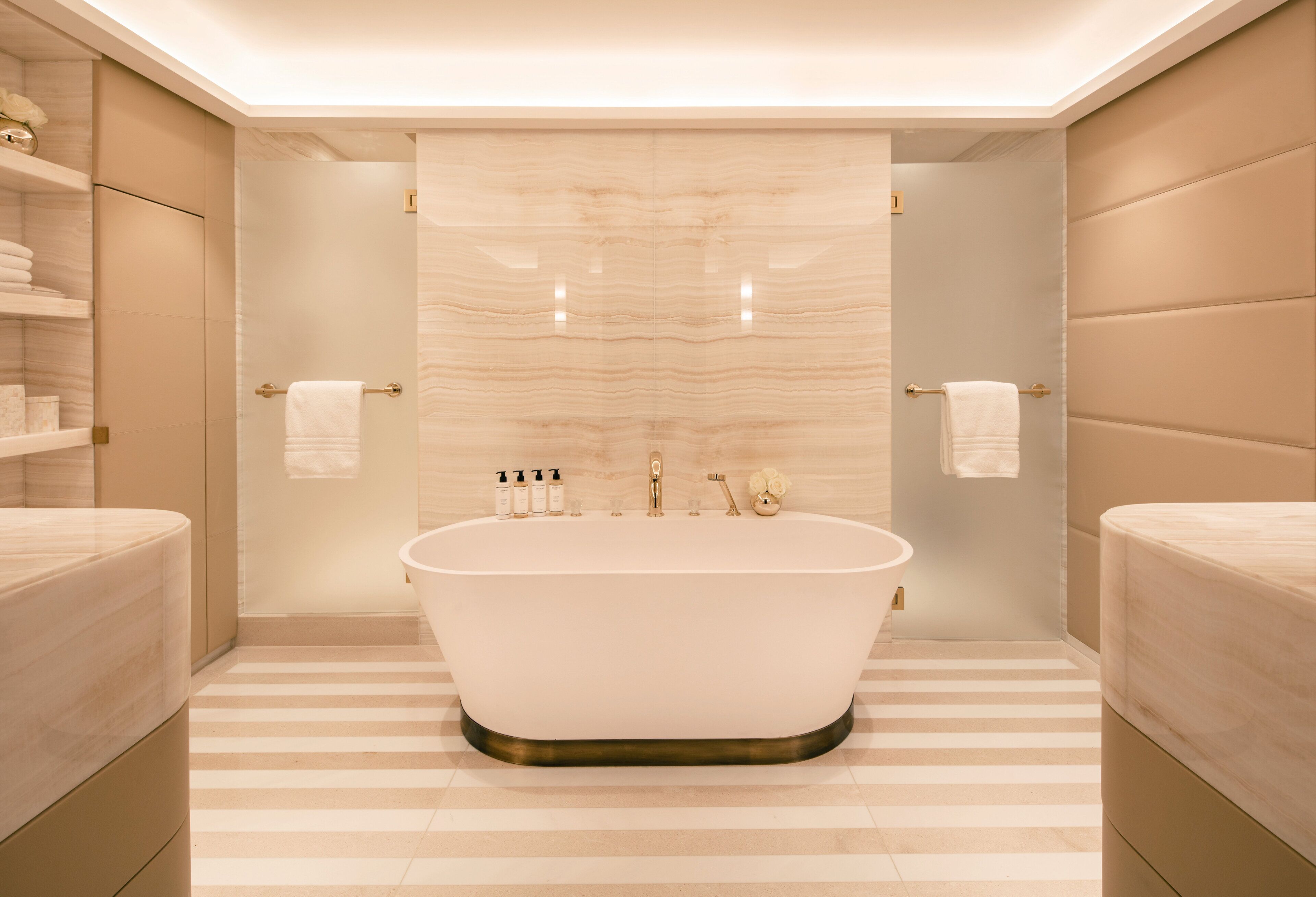 A modern bathroom with a freestanding bathtub, striped floor tiles, and a marble wall.