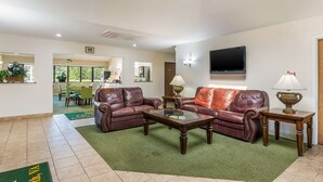 A spacious living room with leather sofas, a coffee table, and a TV mounted on the wall. - Quality Inn Petersburg Fort Lee Area (Petersburg)