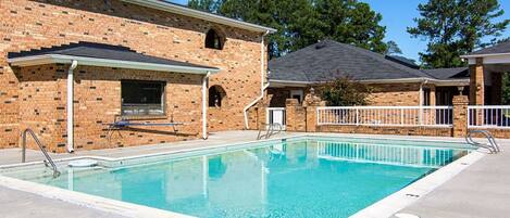 A swimming pool area with a brick building, a covered seating area, and a fenced deck.