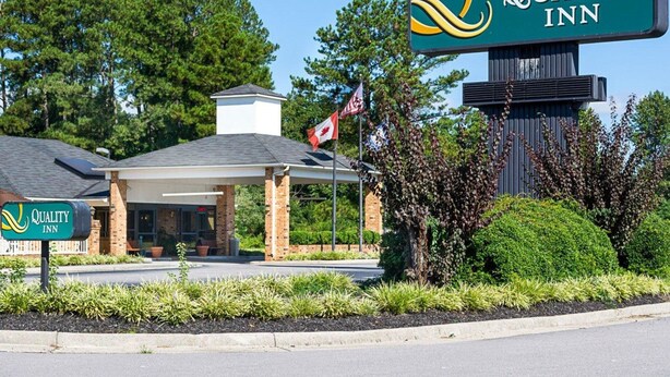 A Quality Inn hotel with a brick facade, a covered entrance, and a flag. - Quality Inn Petersburg Fort Lee Area (Petersburg)