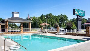 A swimming pool with lounge chairs and a covered seating area, surrounded by a fence and trees. - Quality Inn Petersburg Fort Lee Area (Petersburg)
