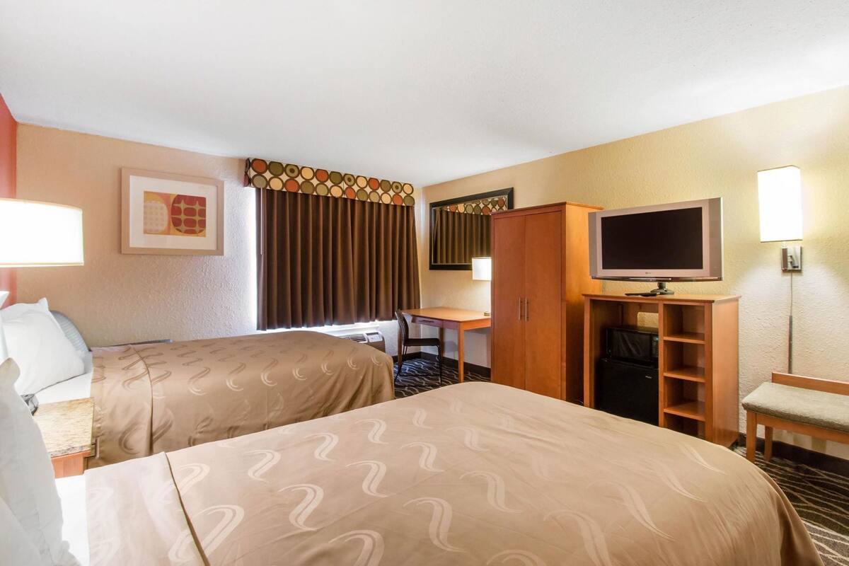 Habitación de hotel con dos camas, un escritorio, televisor y armario.
