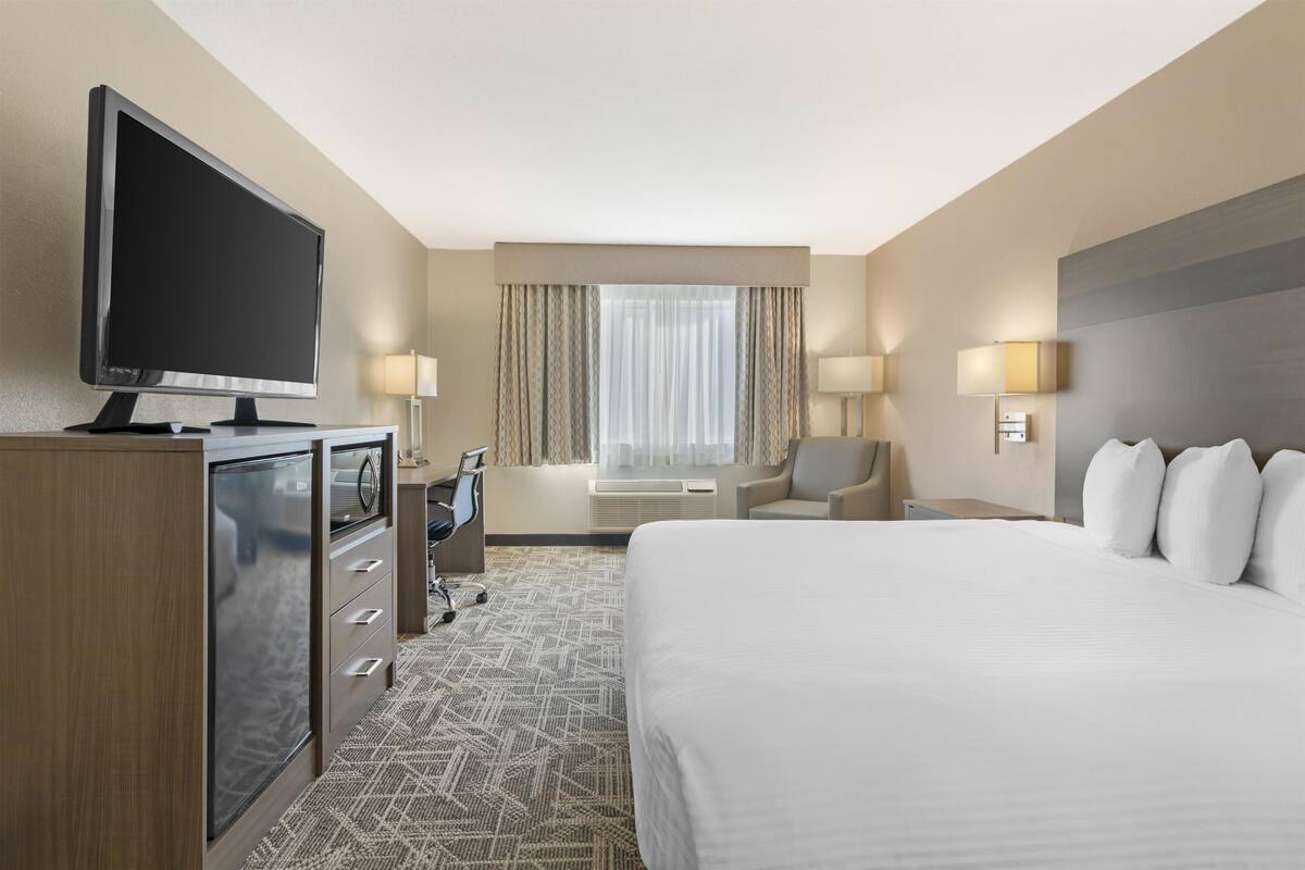 A hotel room with a large bed, a desk with a computer, a television, and a window with curtains.