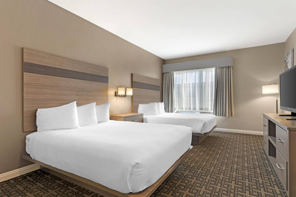 A hotel room with two beds, a television, a desk, and a window with curtains.
