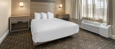 A hotel room with a large bed, two bedside tables, a wall-mounted heater, and a window with curtains.