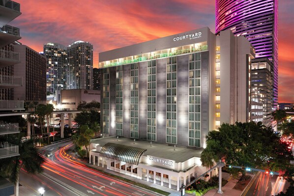 Un hôtel moderne, reconnaissable à son grand panneau « Courtyard by Marriott », à ses larges fenêtres et à sa toiture aux lignes courbes.