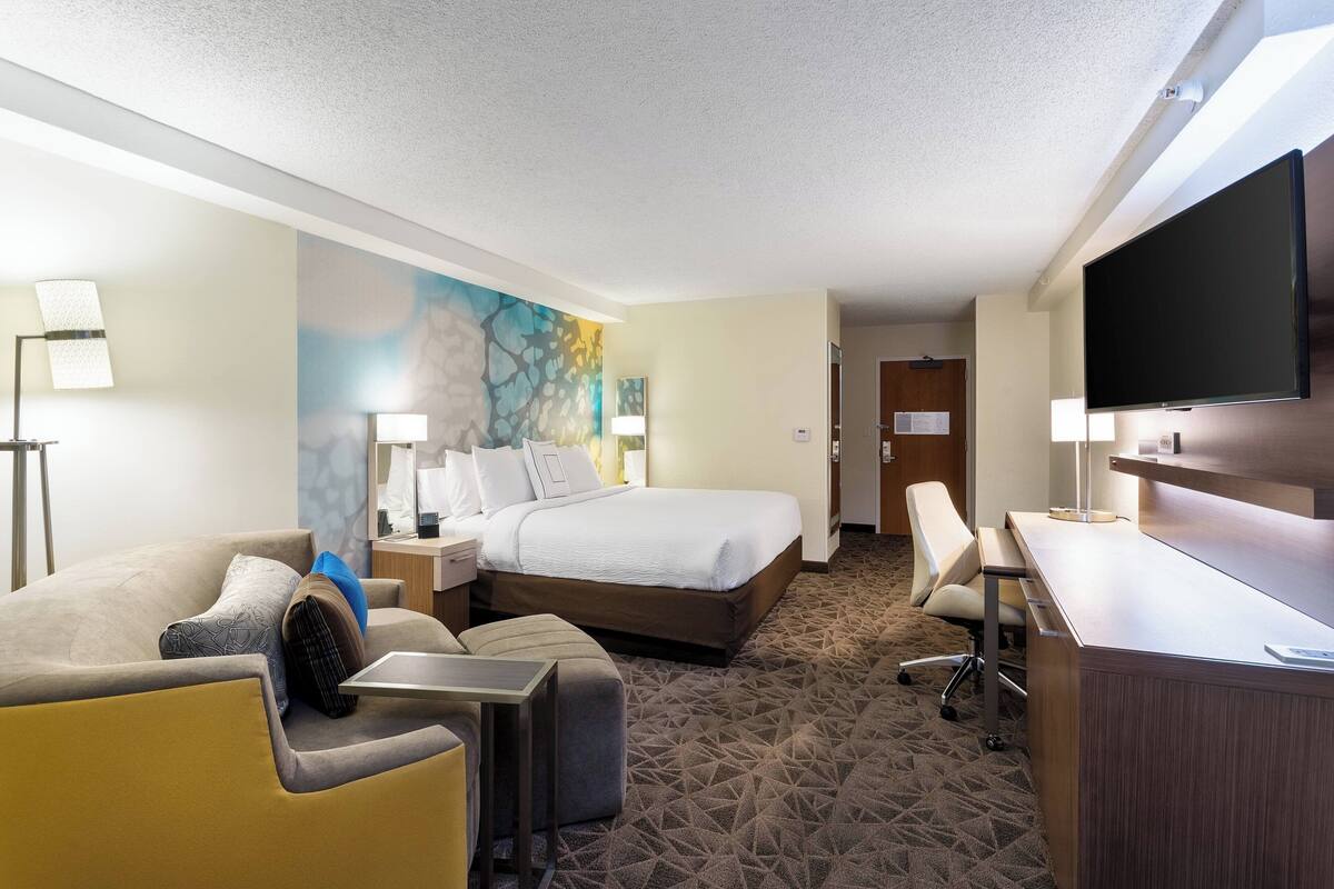 Une chambre d’hôtel équipée d’un lit, d’un bureau, d’une chaise, d’un canapé et d’une télévision.