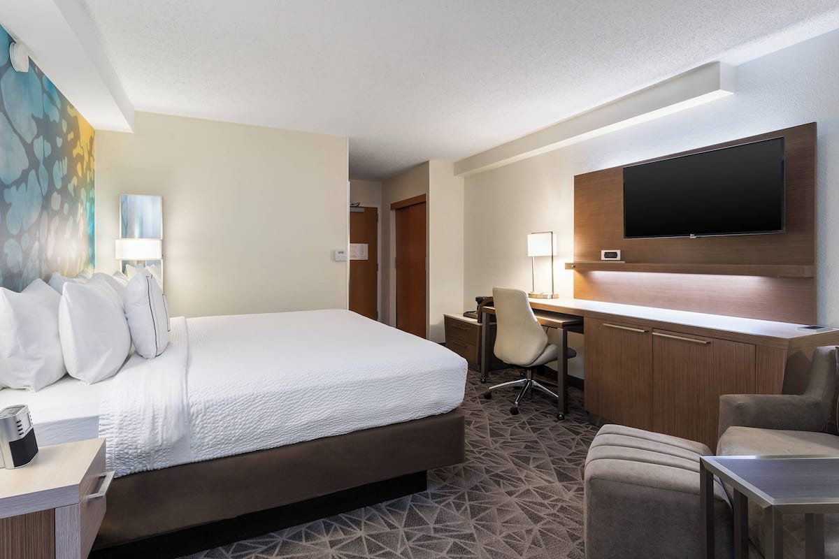 Une chambre d’hôtel avec un grand lit, un bureau avec une chaise, un téléviseur à écran plat fixé au mur et un tableau accroché au mur.